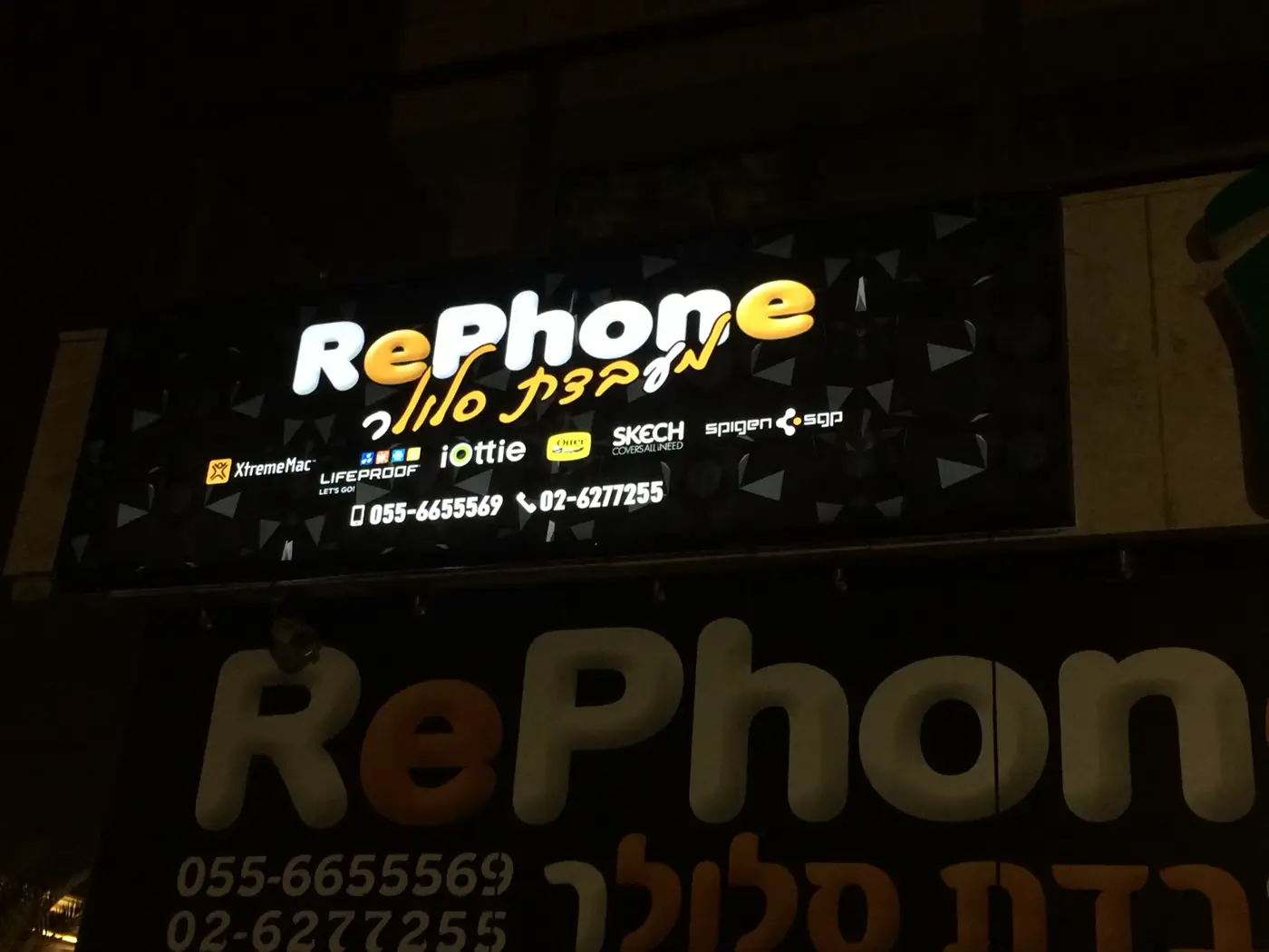 ארגז מואר שחור עם לוגו צבעוני, לוגואים של מותגים ומספרי טלפון, מעל חנות סלולר בלילה