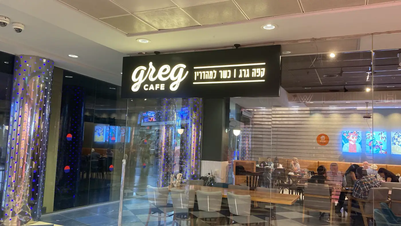 ארגז קאט אאוט שחור תלוי מעל כניסה לבית קפה בקניון, לוגו כתב יד ושורת טקסט עברית מוארים