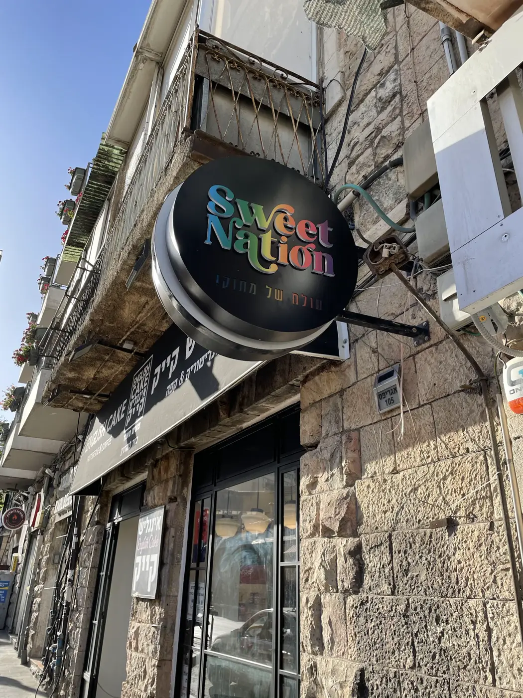 שלט דגל עגול שחור עם אותיות בנויות בצבעי קשת בולטות, על בניין אבן ברחוב