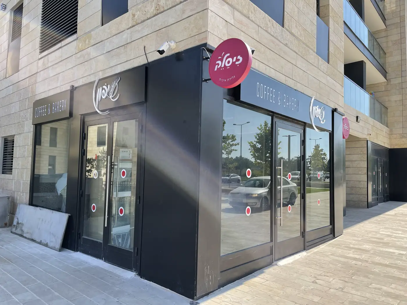 צילום רחב של פינה מסחרית: שלטי דגל עגולים ורודים יחד עם פאנל שחור ואותיות לבנות של מאפייה