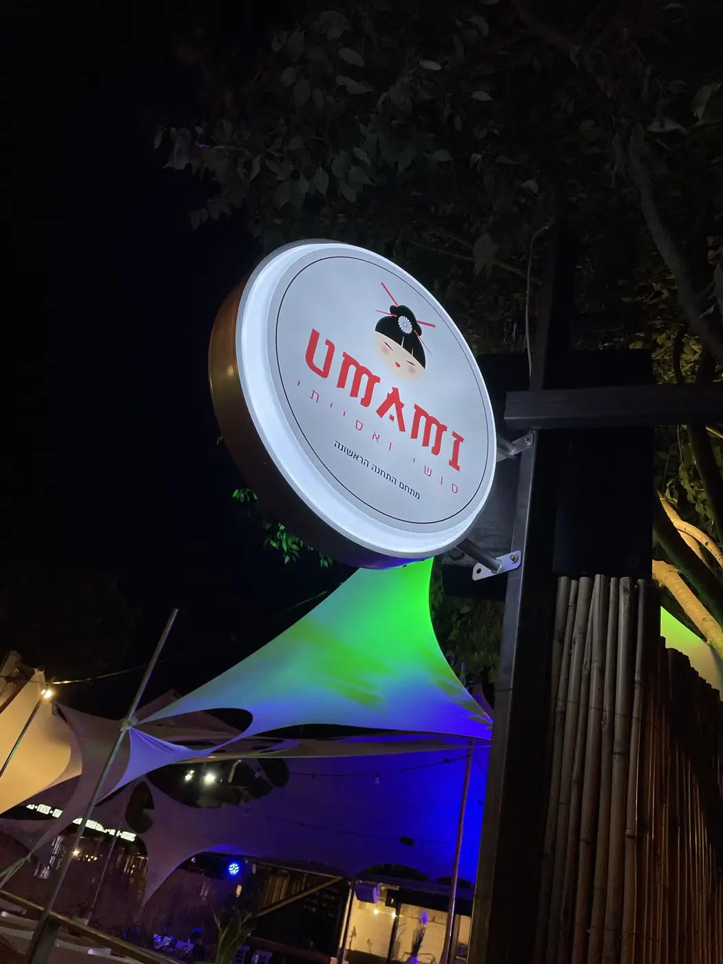 שלט דגל עגול מואר עם לוגו דמות גיישה, בלילה במתחם מסעדות פתוח