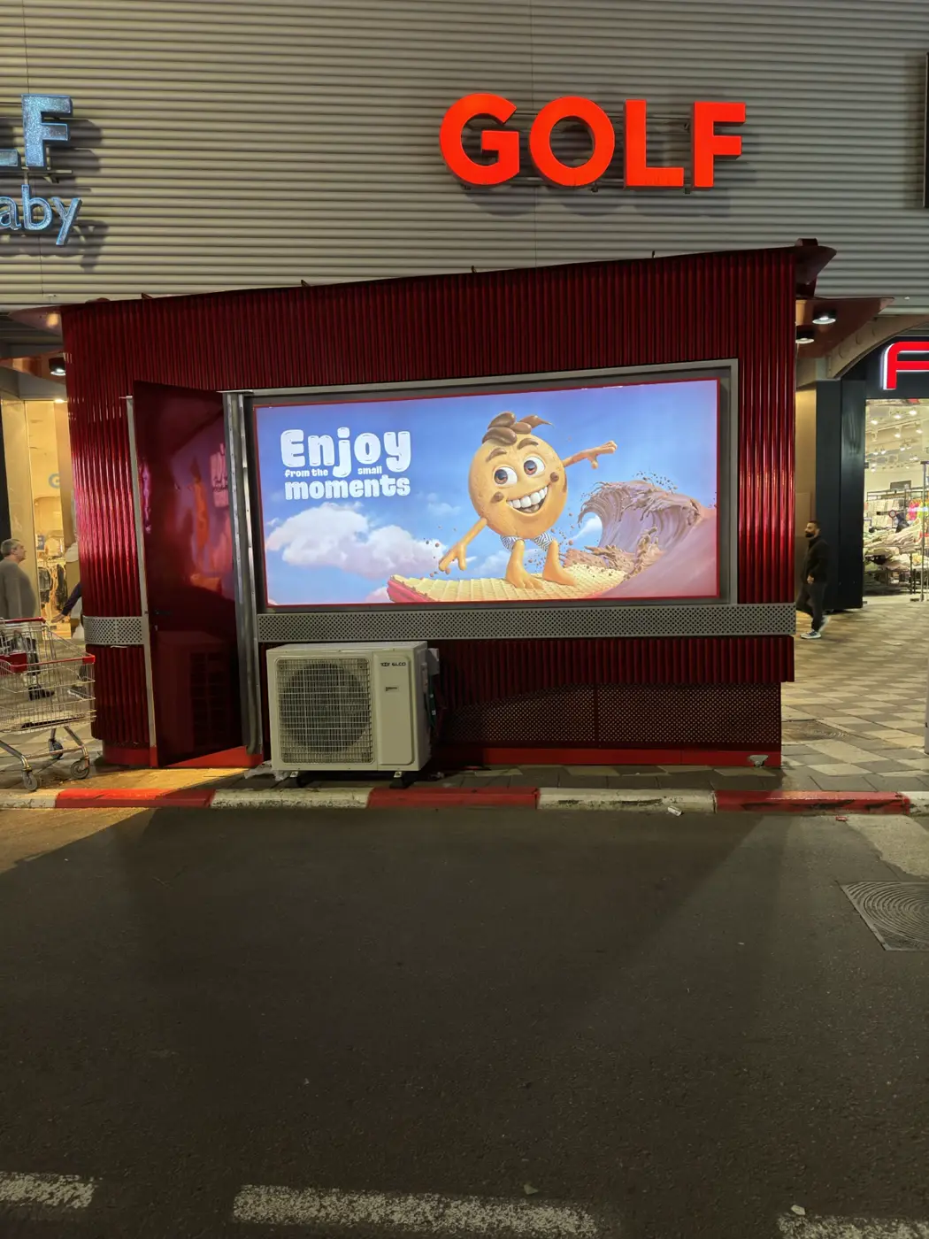 ארגז מואר גדול עם תמונה צבעונית בחזית של קיוסק אדום ברחוב, בערב