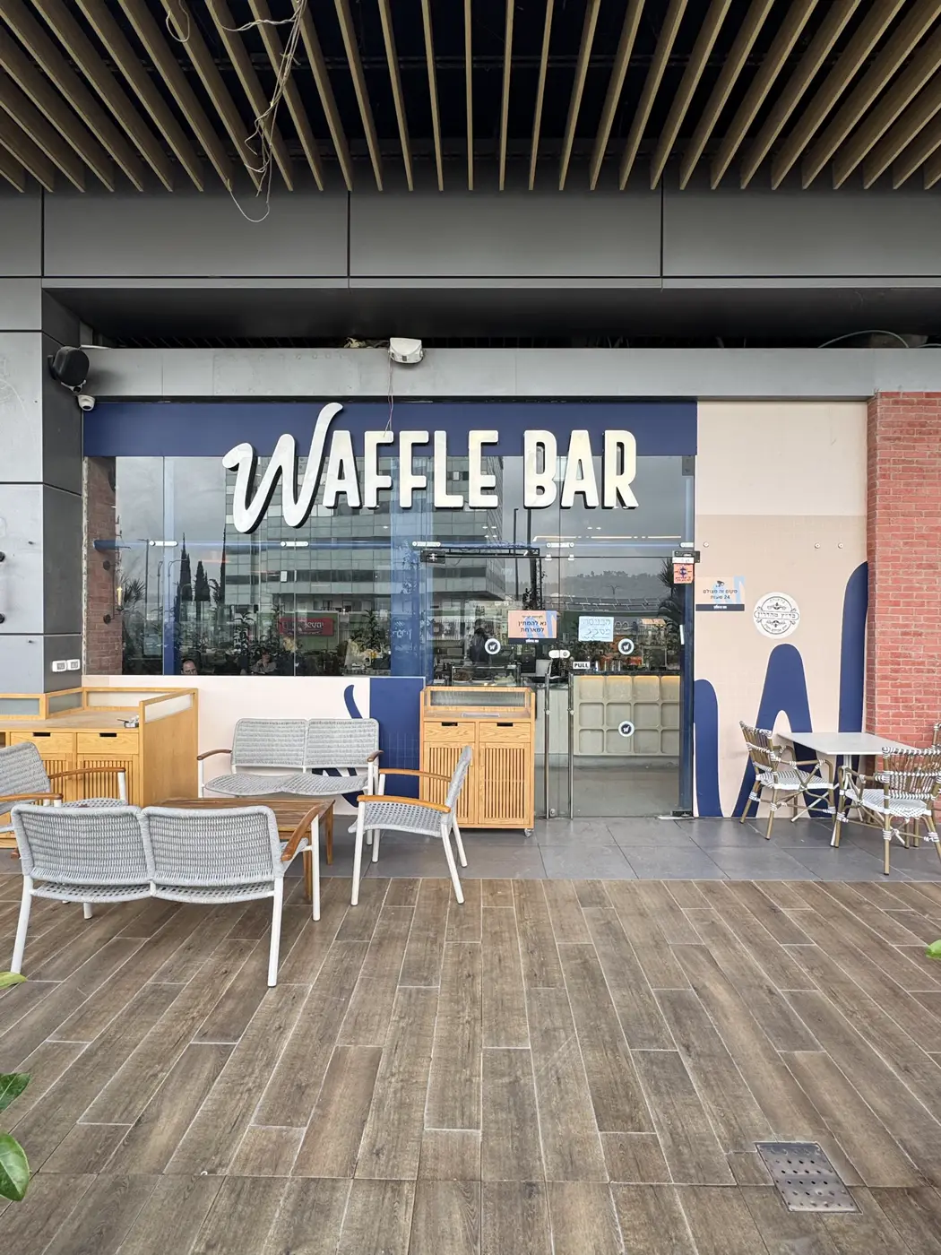 אותיות בנויות לבנות מוארות "WAFFLE BAR" על פס כחול מעל חזית זכוכית של בית קפה
