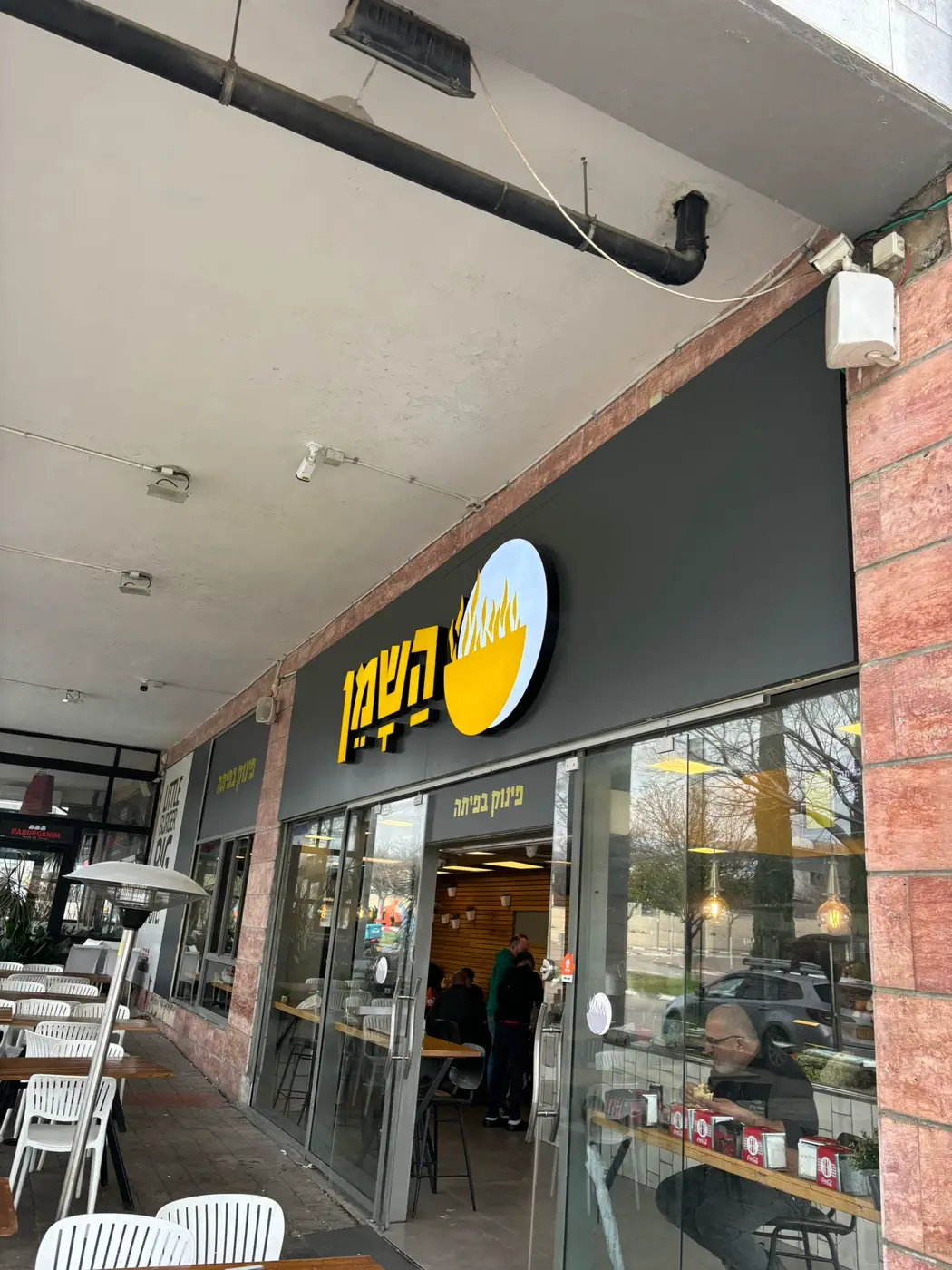 אותיות עבריות צהובות בנויות ולוגו עגול מואר על פאנל שחור מעל חזית זכוכית של מסעדה