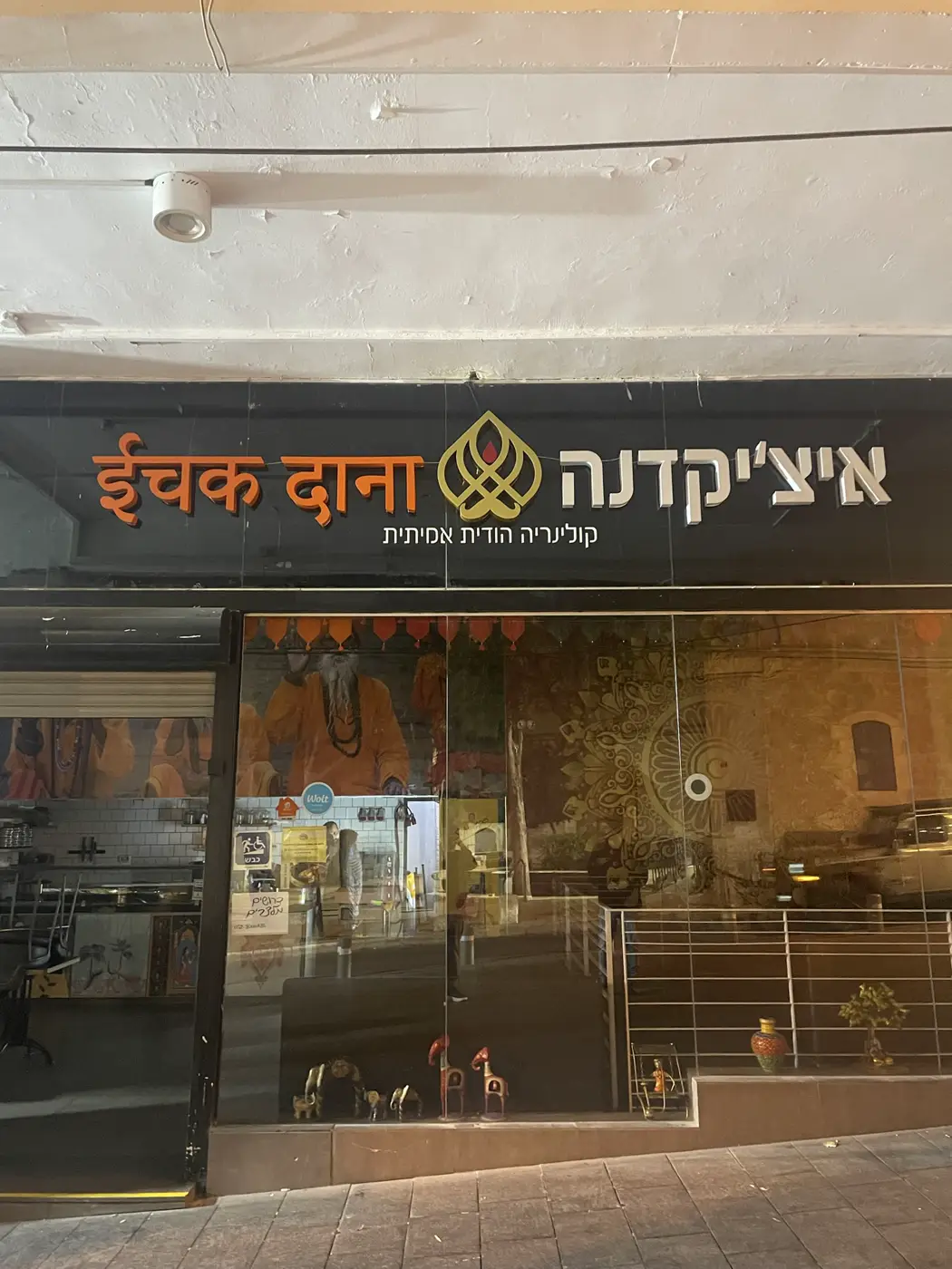 אותיות בנויות בעברית ובהינדית בכתום ולבן, ולוגו זהב במרכז, על פאנל שחור מעל חזית מסעדה