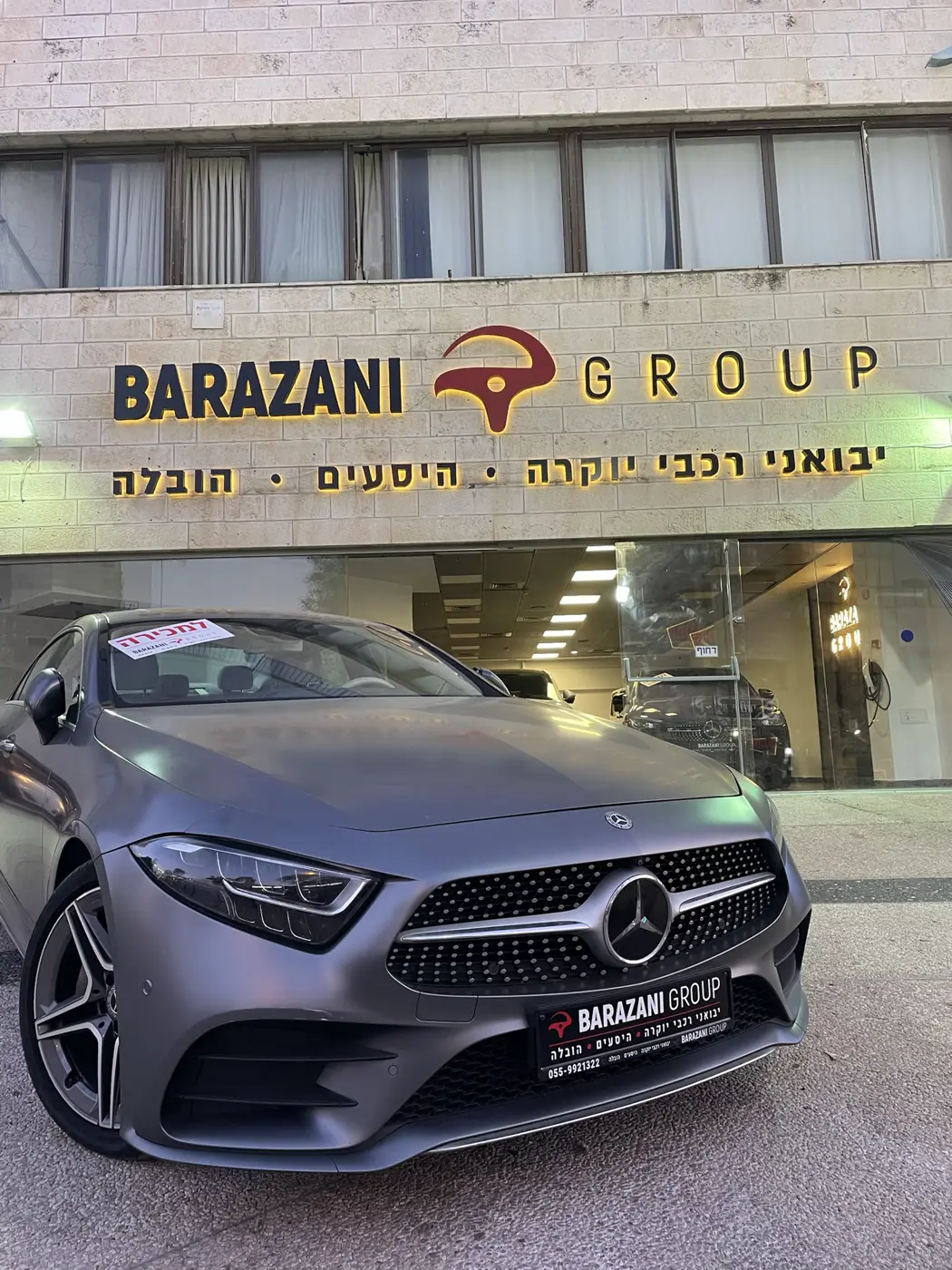 אותיות שחורות ולוגו אדום עם הילה צהובה-חמה על חזית אבן של אולם תצוגה לרכבי יוקרה, עם שורת טקסט בעברית