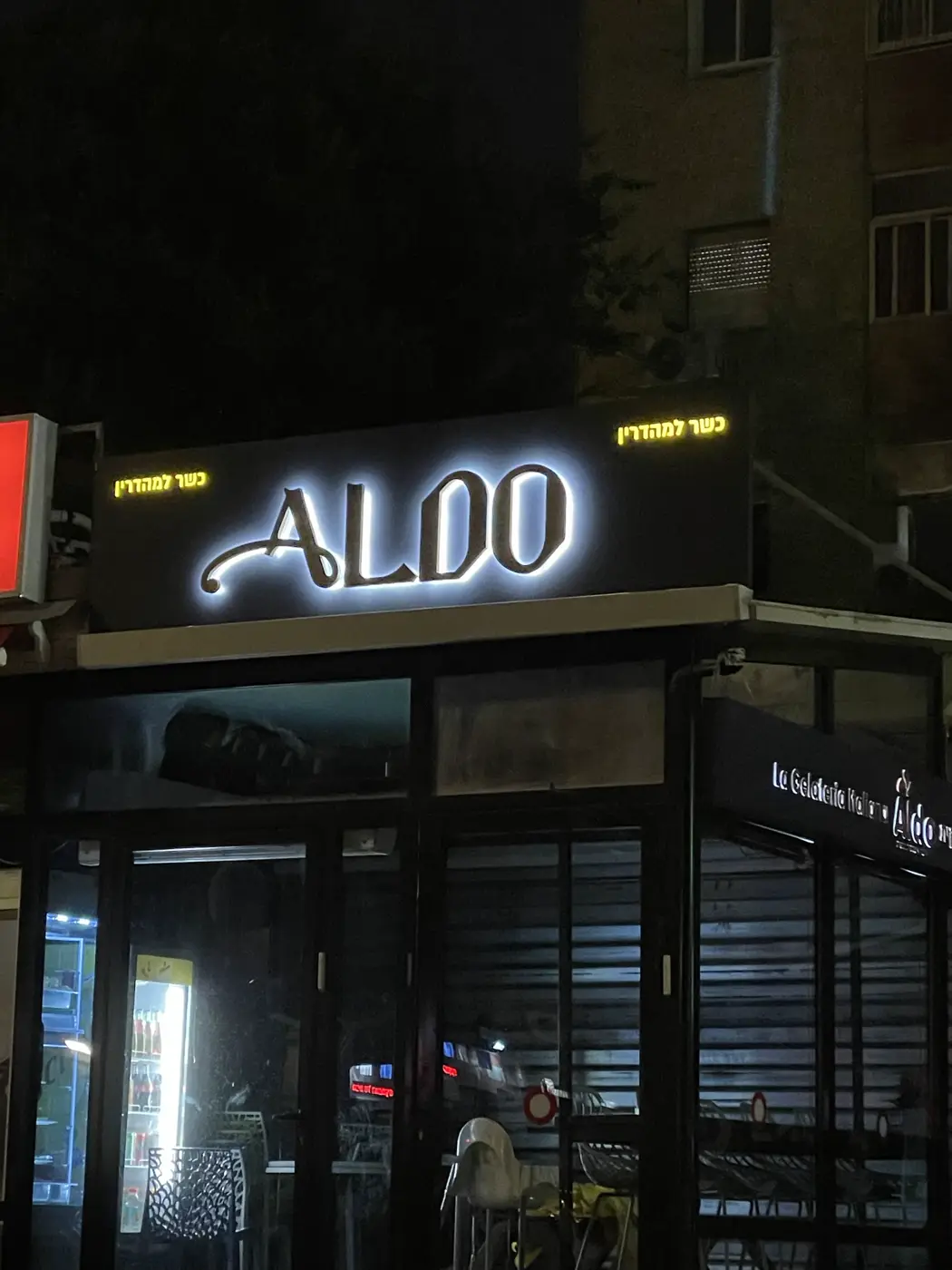 אותיות מעוצבות עם הילה לבנה על פאנל שחור מעל גלידריה, ו"כשר למהדרין" מואר בצהוב בצדדים