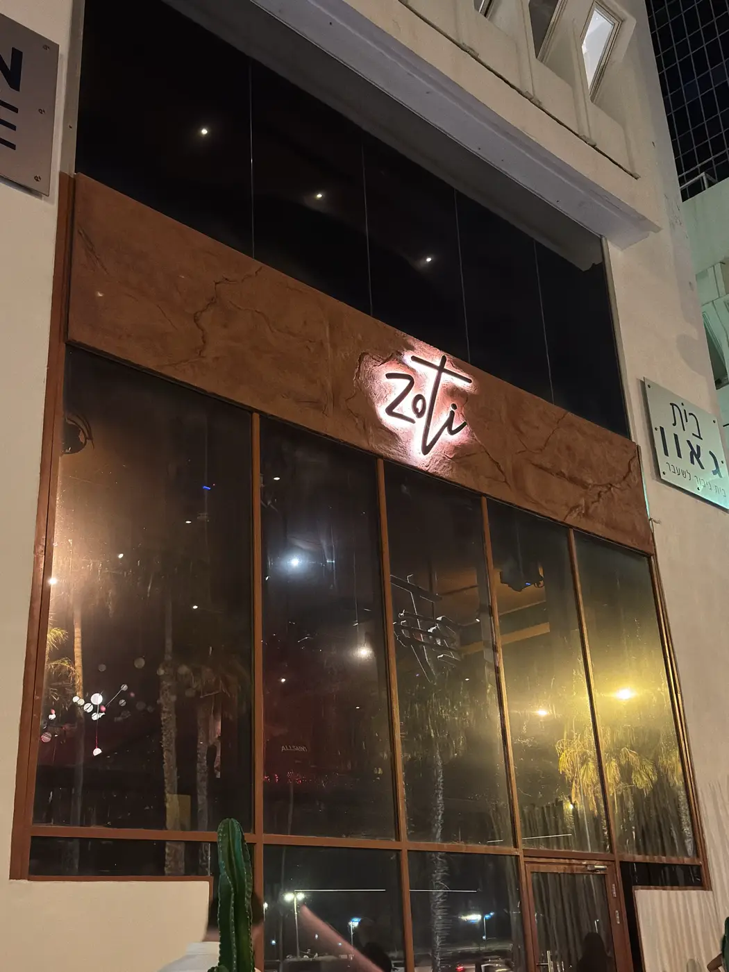 חזית מסעדה מזווית: לוגו כתב יד עם הילה חמה על פס חיפוי חום, רואים איך השלט עובד מהרחוב