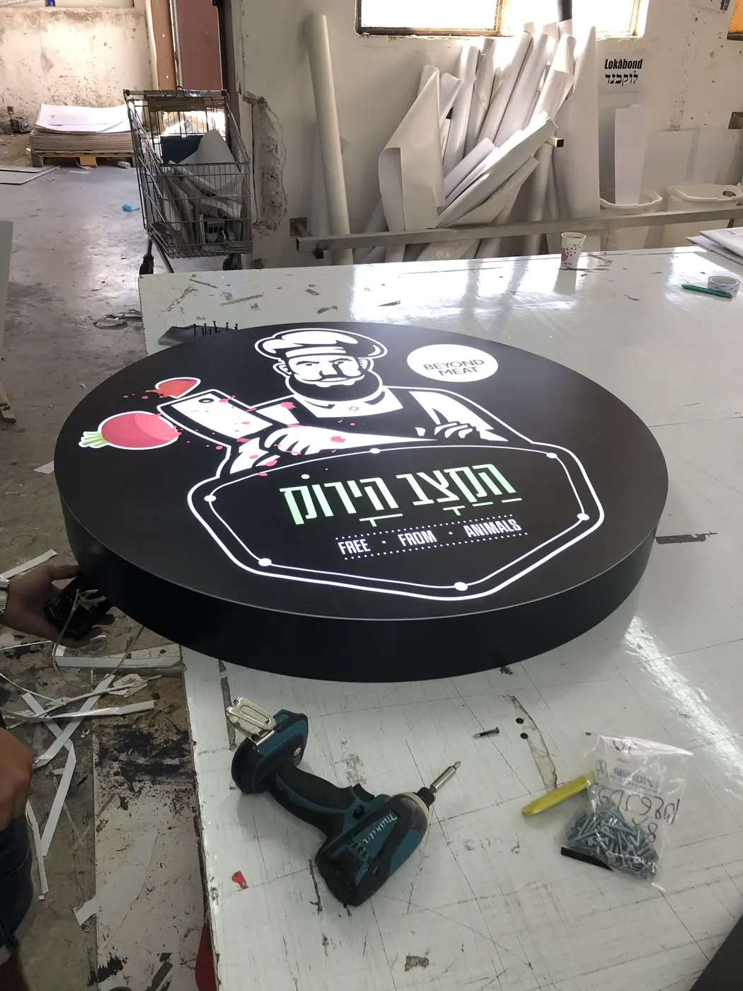 ארגז מואר עגול שחור עם איור קצב ולוגו עברי ירוק, דולק במפעל